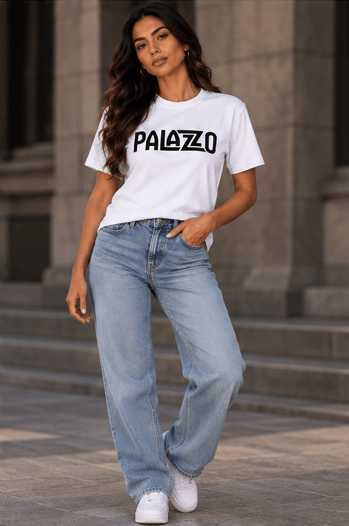 Frau in weißem T-Shirt mit 'PALAZZO'-Schrift, lockere Jeans, urbanes Umfeld, entspannter Streetwear-Stil, moderne Mode