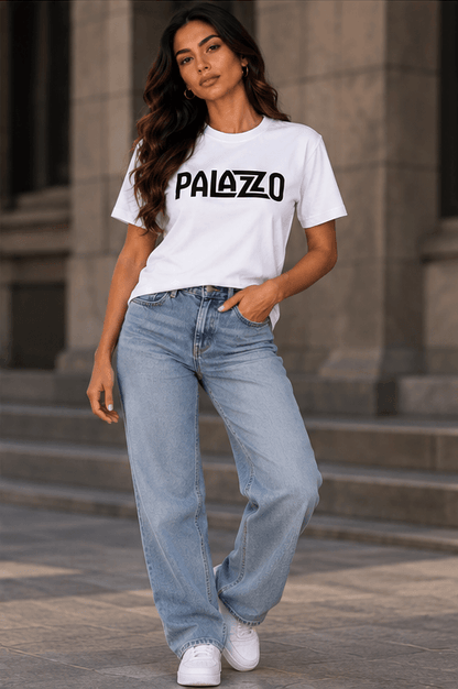 Frau in weißem T-Shirt mit 'PALAZZO'-Schrift, lockere Jeans, urbanes Umfeld, entspannter Streetwear-Stil, moderne Mode